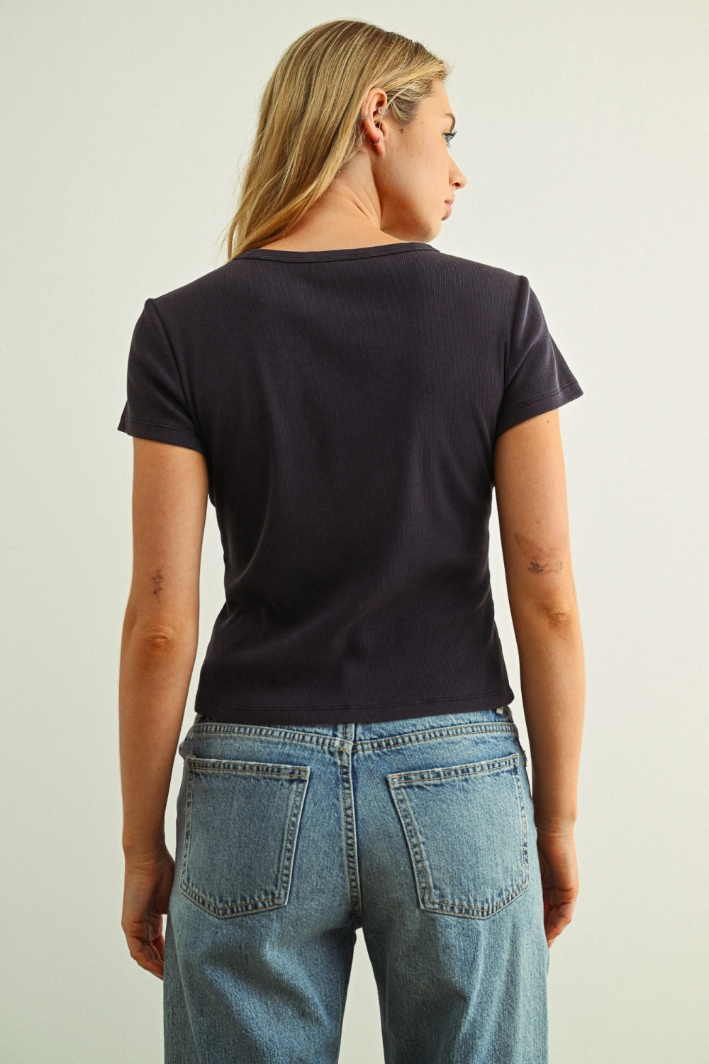Person wearing a black t-shirt and blue jeans on a plain background
