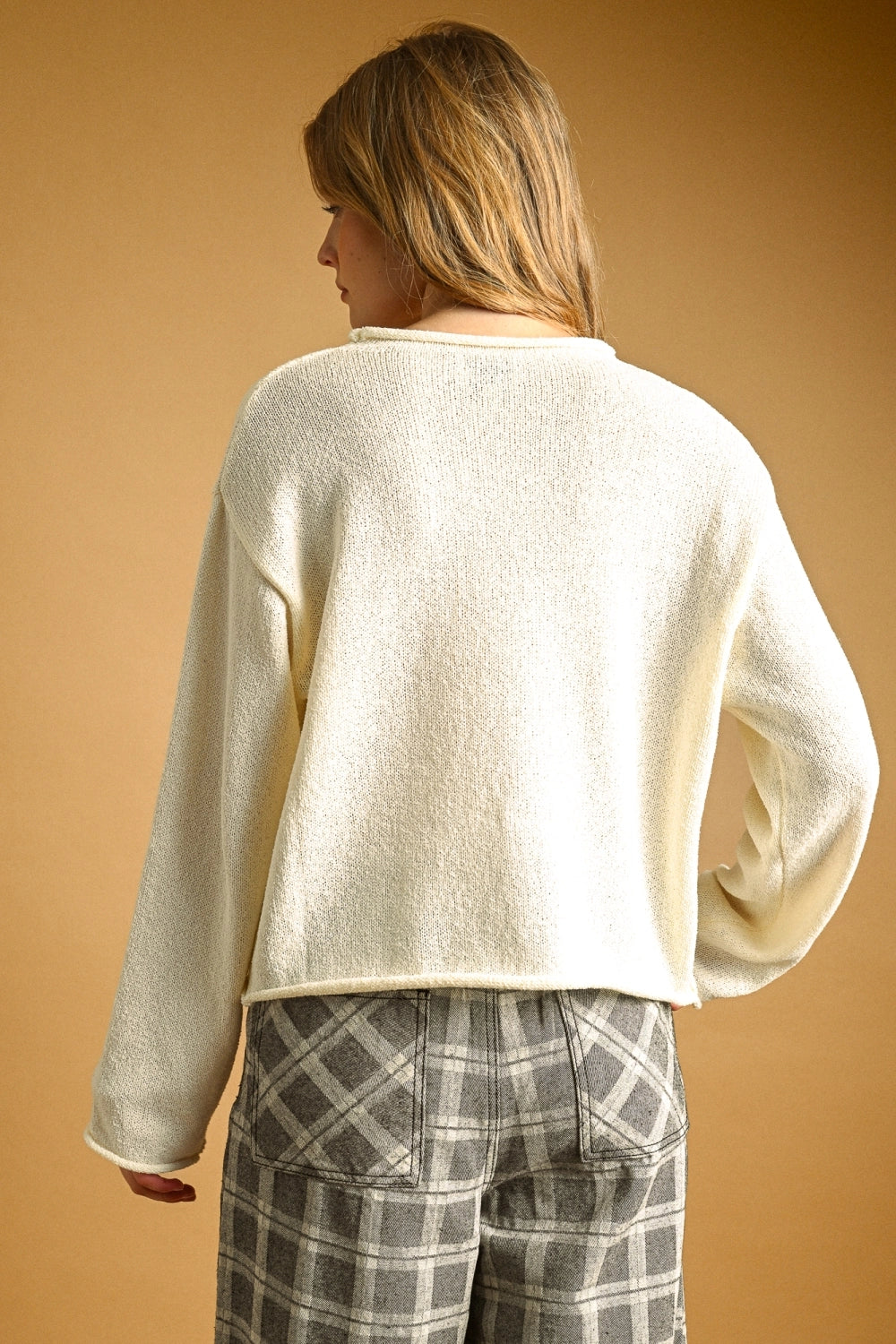 Woman wearing a cream sweater and plaid pants against a beige background