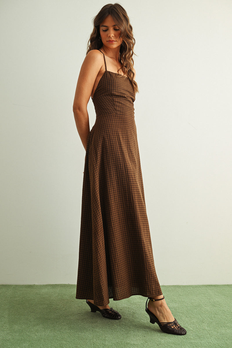 Woman wearing a brown checkered dress standing against a plain background