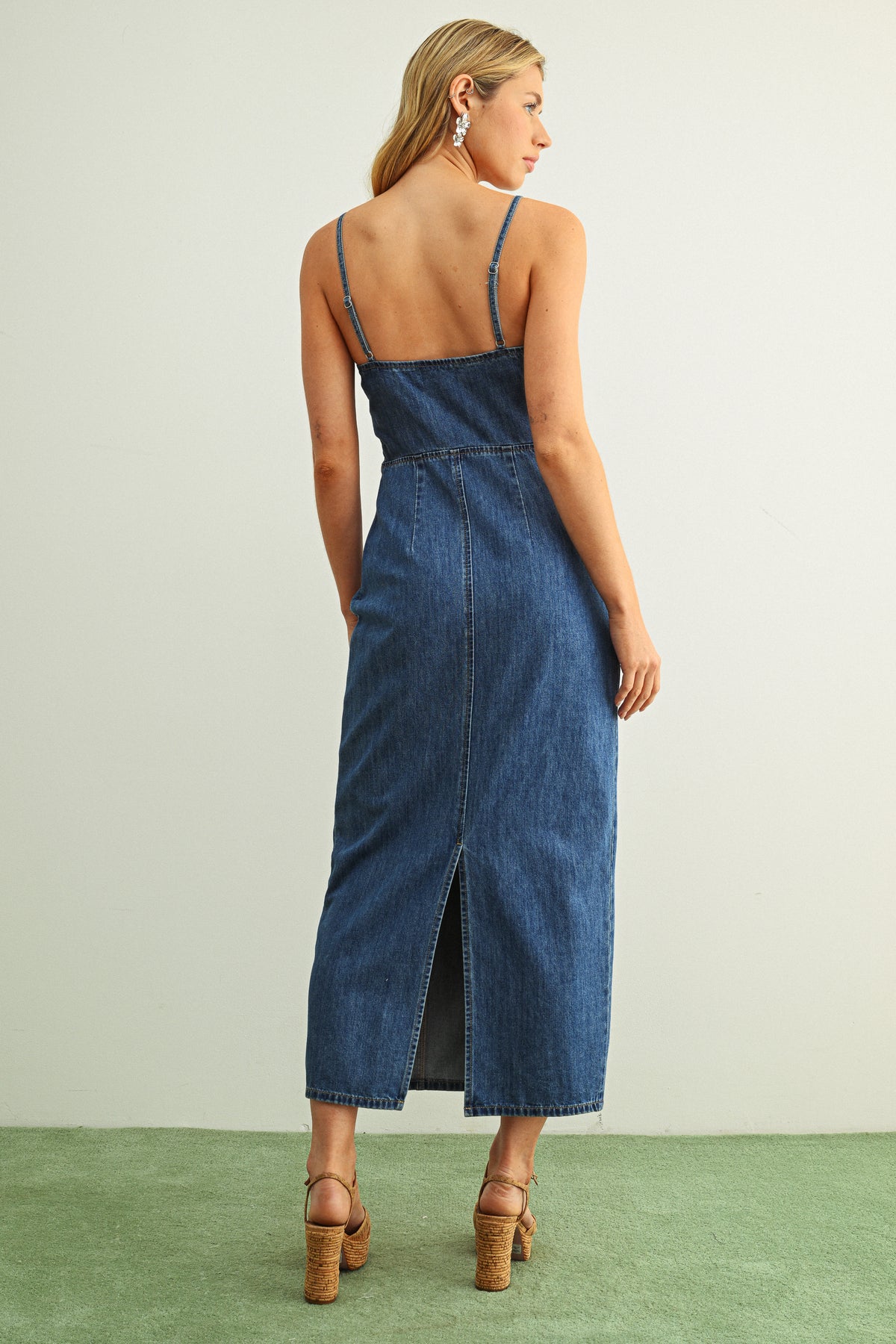 Woman wearing a blue denim dress with a backless design on a plain background