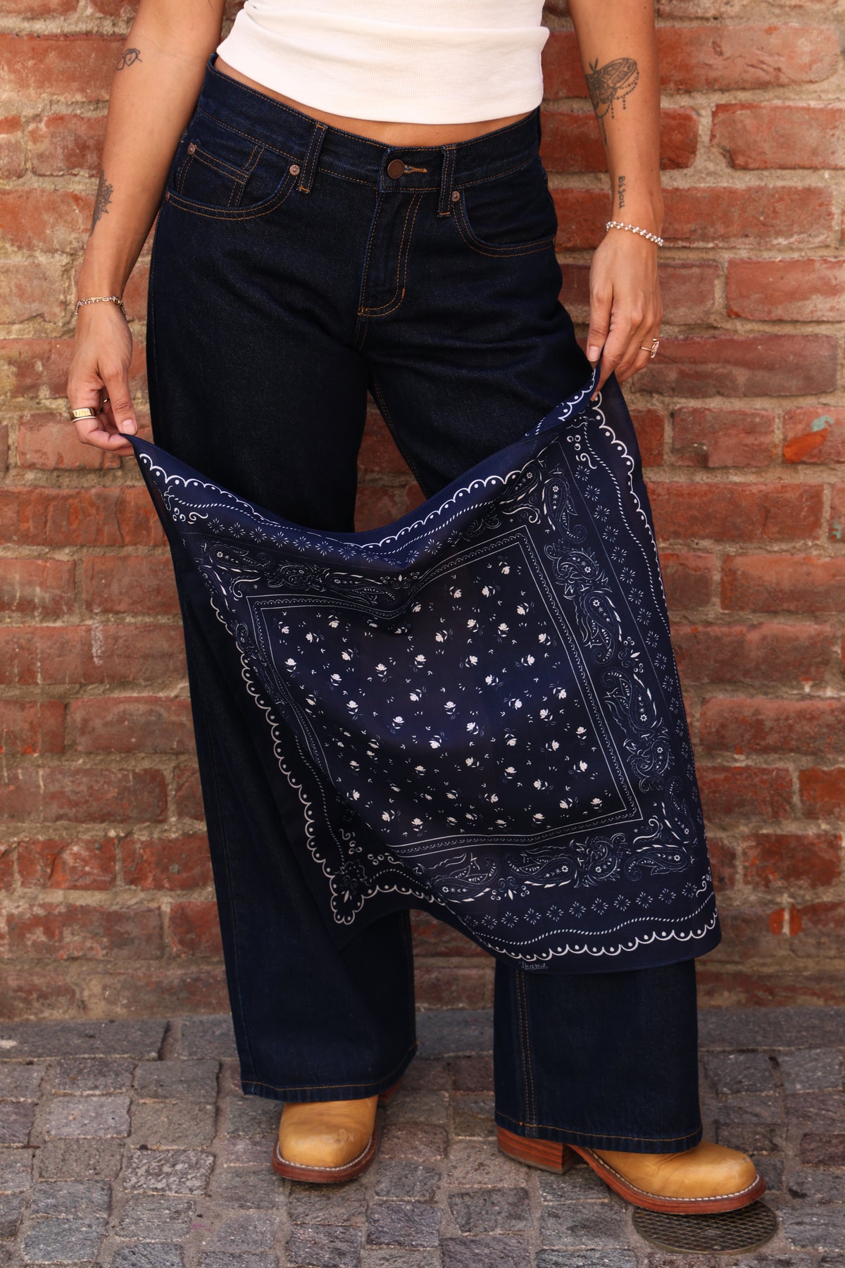Woman standing holding a bandana against a brick wall.