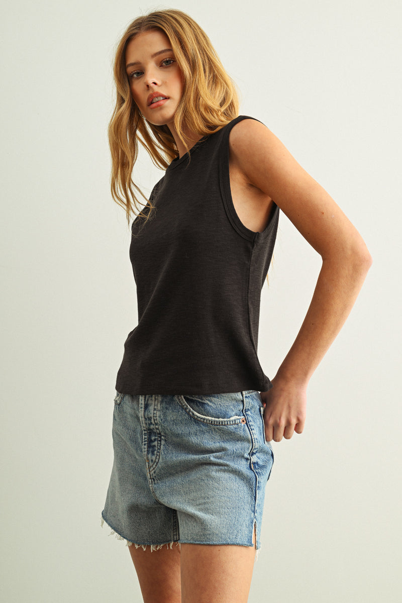 A woman wearing a black cotton tank with jeans in front of a white background
