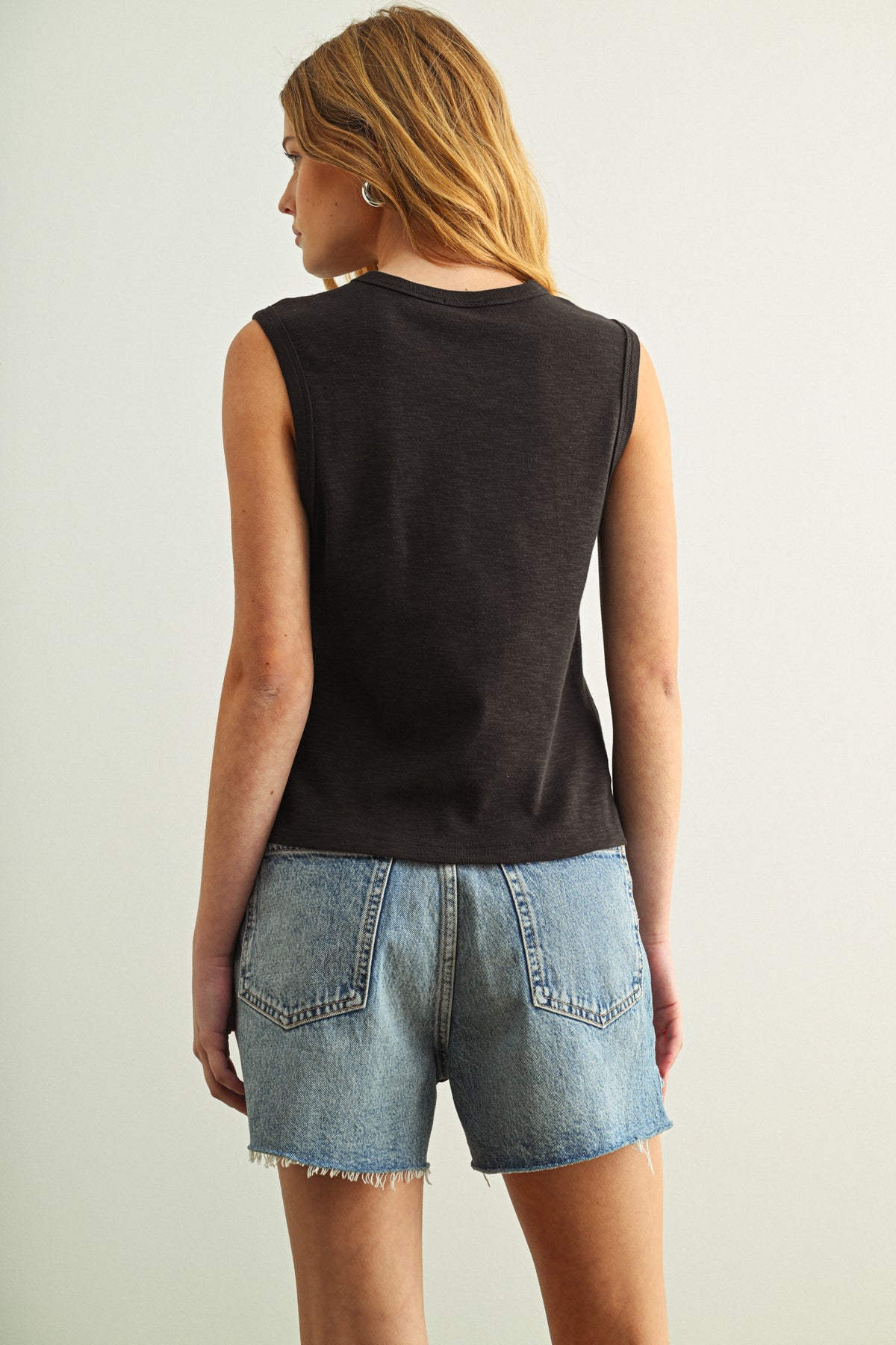 A woman wearing a black cotton tank with jeans in front of a white background
