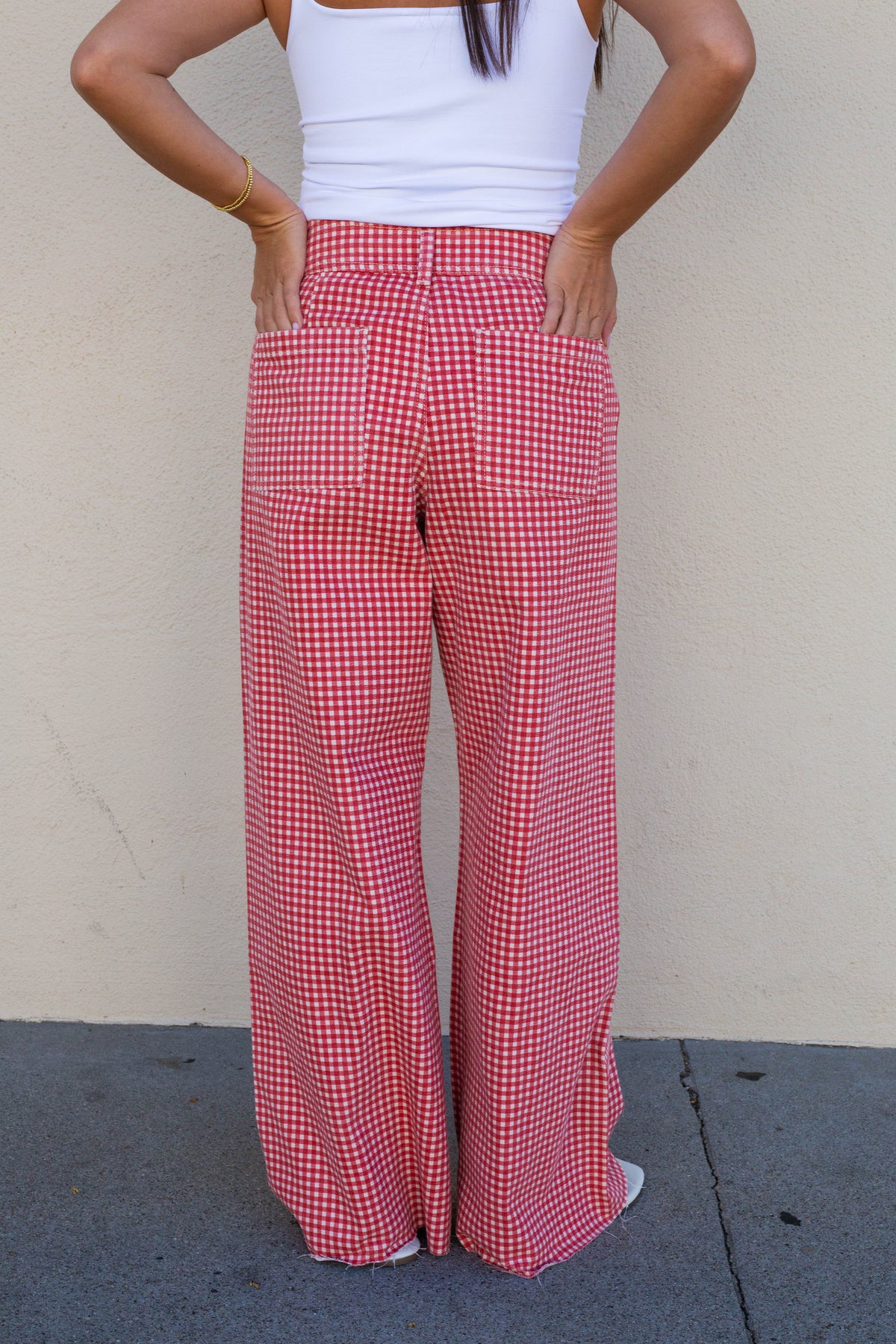 A person wearing red and white gingham wide-leg pants with a white tank top, standing against a beige stucco wall.