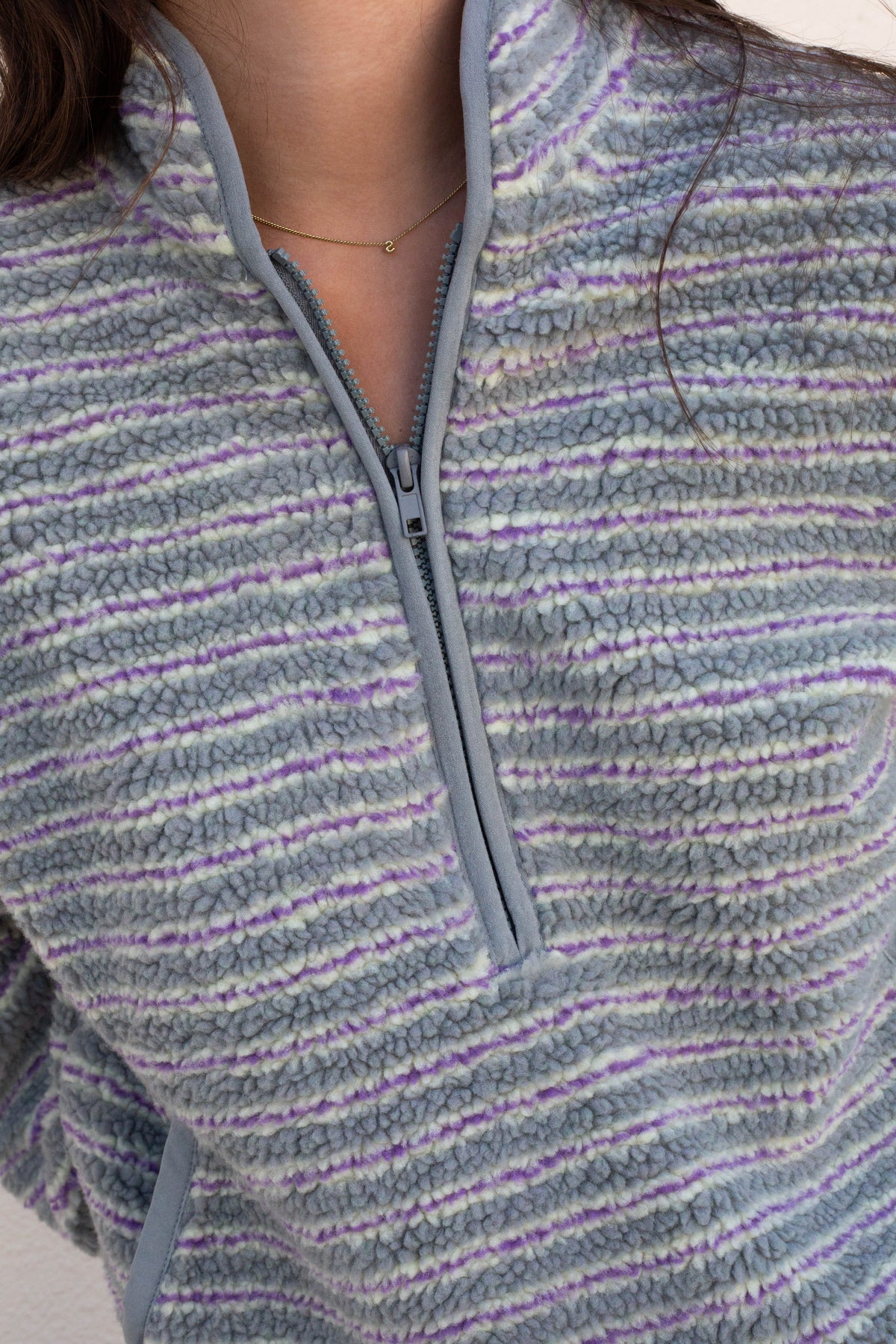 Close-up of a person wearing a fuzzy quarter-zip fleece pullover with horizontal gray, purple, and white stripes.