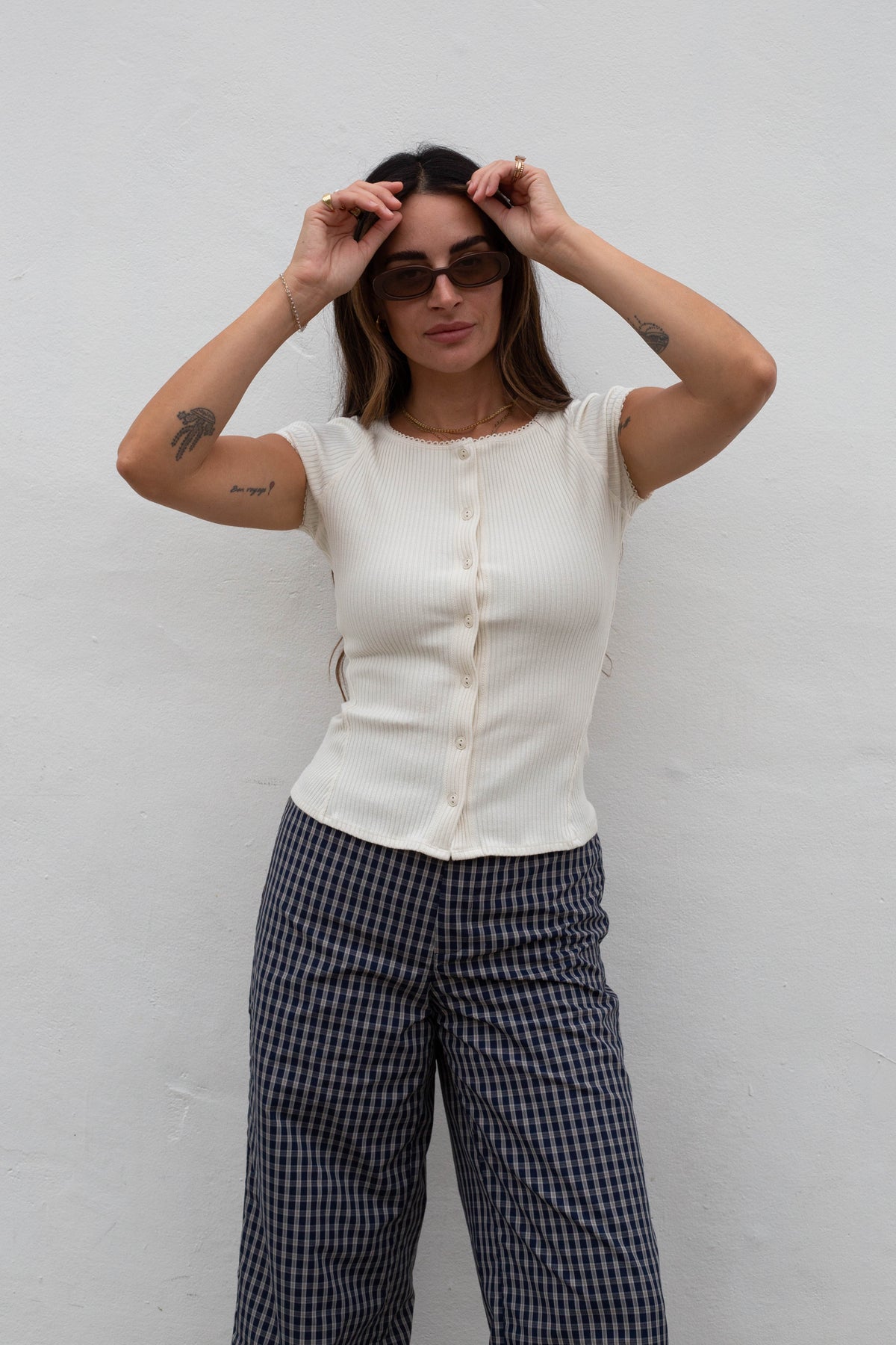 A woman wearing a cream ribbed short-sleeve button-front top and navy-and-white gingham wide-leg pants, posing against a white wall.