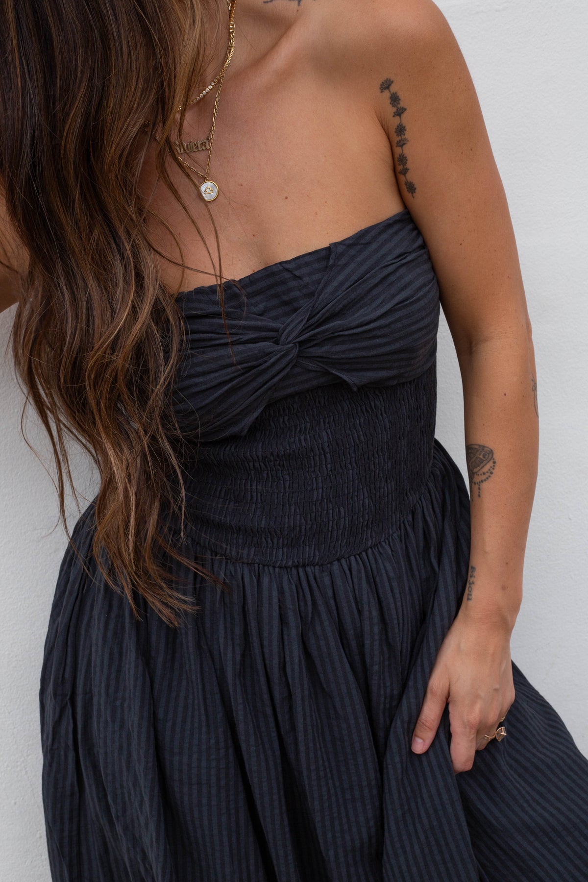 A close-up of a woman wearing a dark navy blue strapless pleated dress with a knotted sweetheart neckline and a smocked waistband.