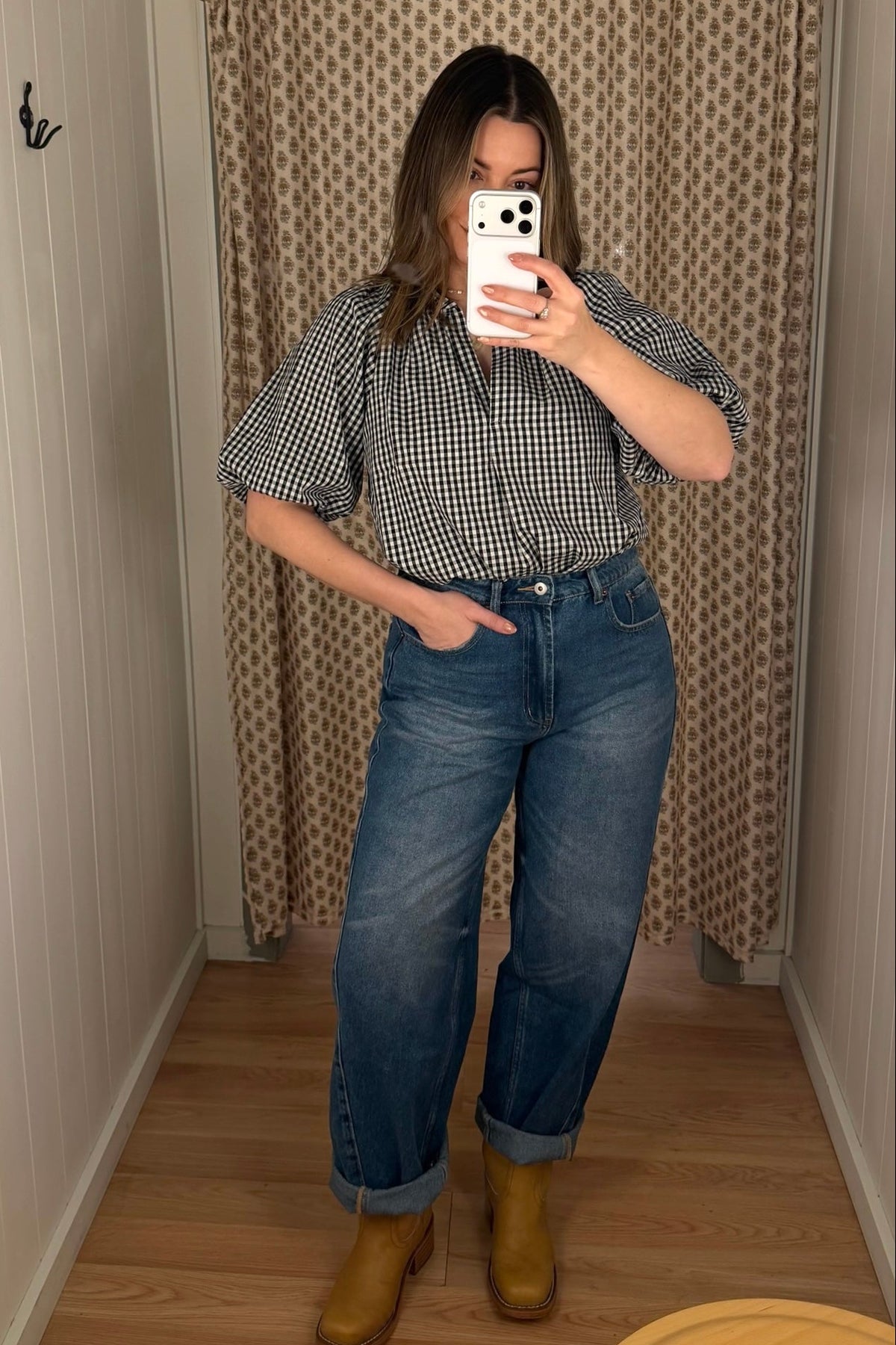 Person taking a mirror selfie wearing a checkered shirt, blue jeans, and yellow boots in a room with a patterned curtain.