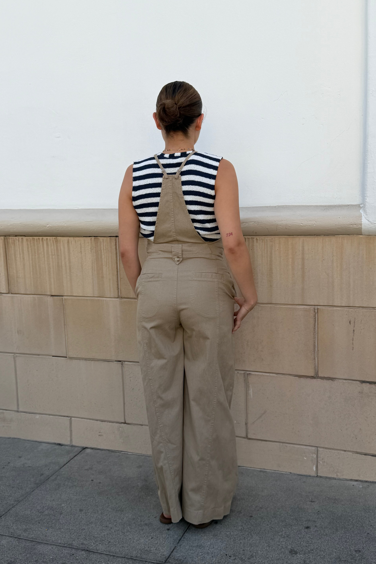 Person wearing beige overalls and a striped shirt standing against a light-colored wall.