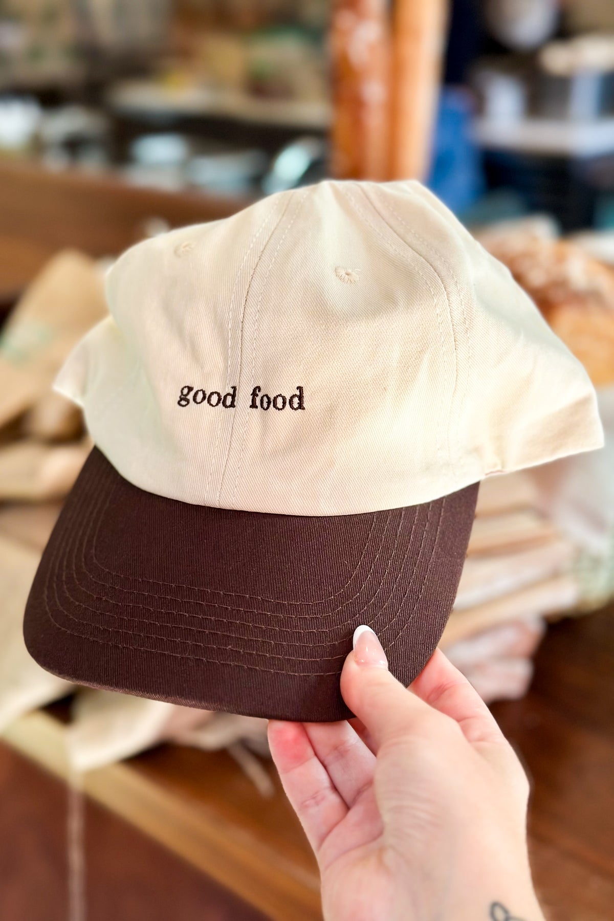 Cap with 'good food' text held by a hand in a store setting