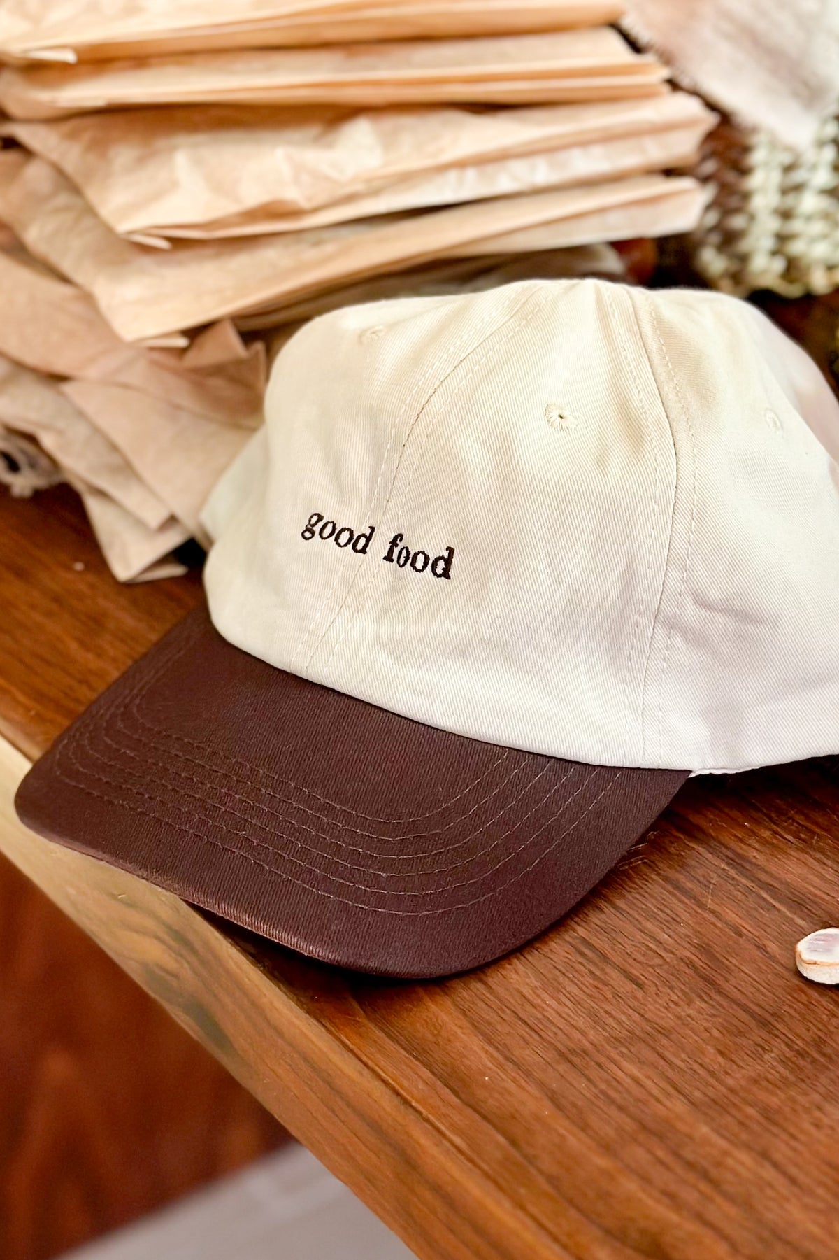 Beige and brown cap with 'good food' text on a wooden surface