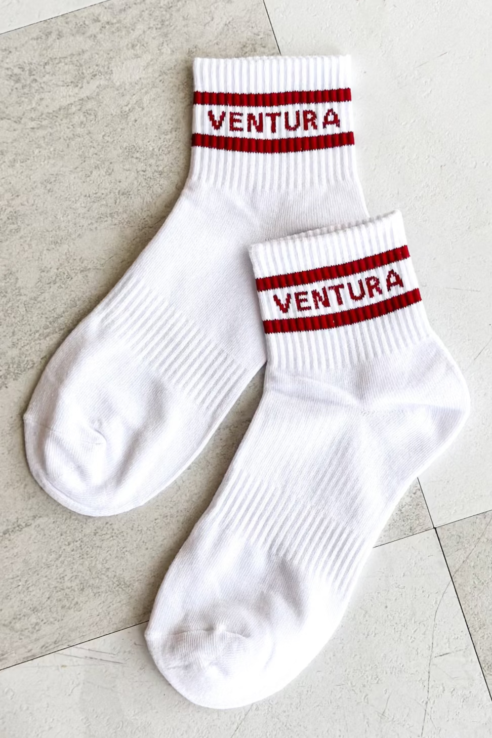 White socks with red stripes and 'Ventura' branding on a tiled floor.