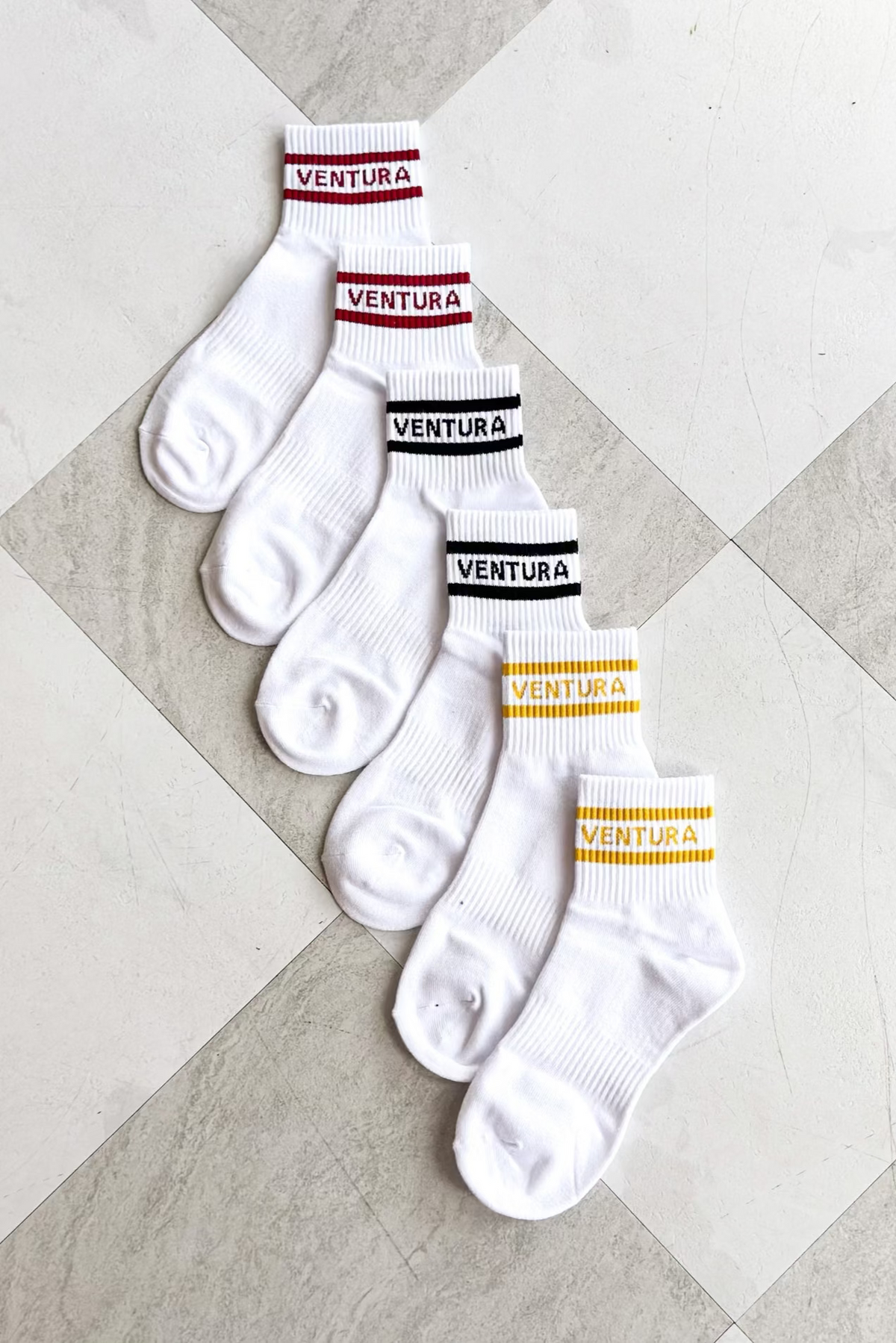 Set of white socks with 'Ventura' branding on a checkered floor.