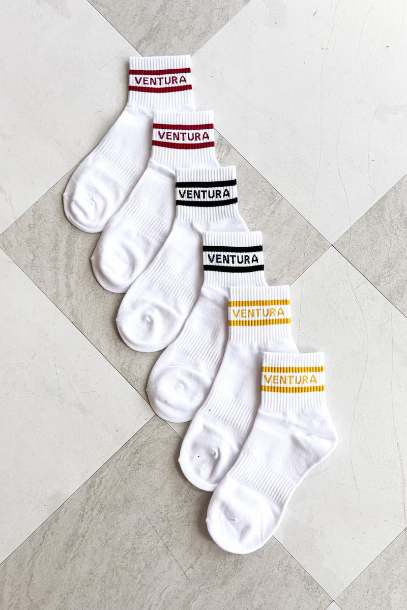 Set of white socks with 'Ventura' branding on a checkered floor.