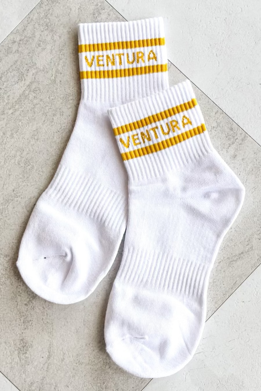 White socks with yellow stripes and 'Ventura' branding on a tiled floor.