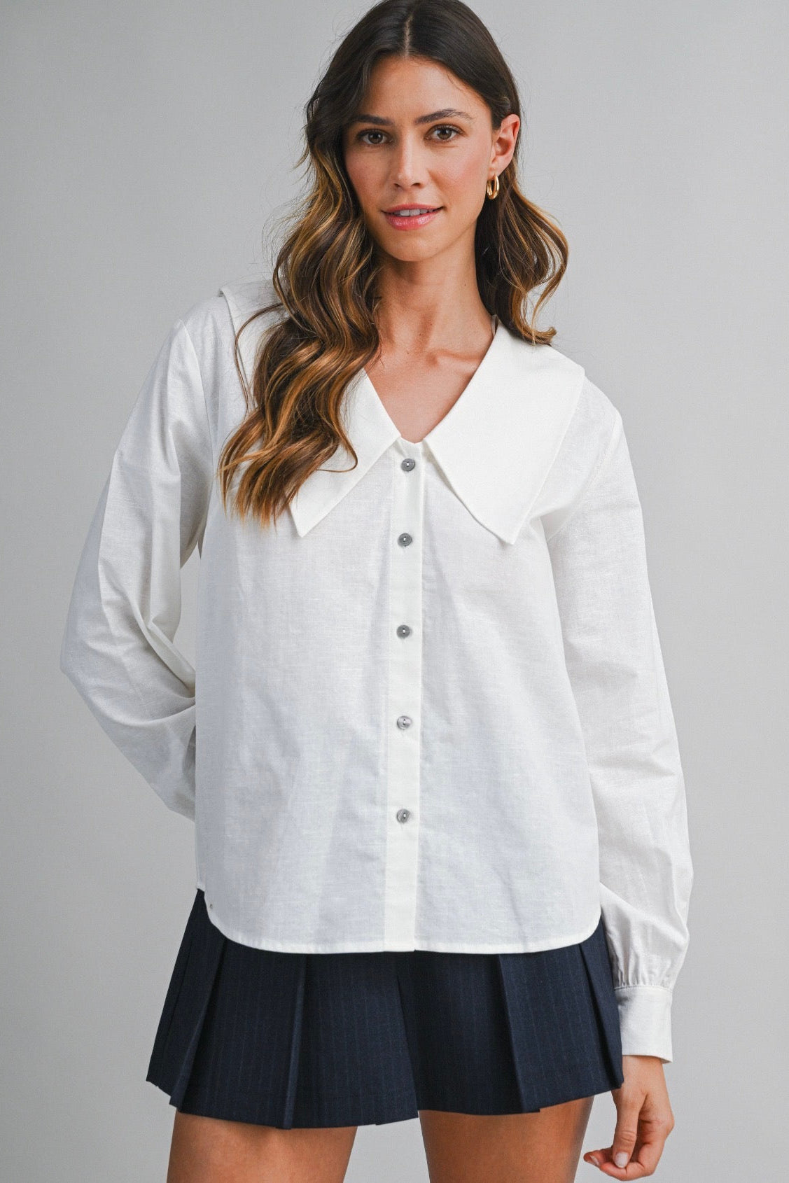 Woman wearing a white blouse and navy skirt on a gray background