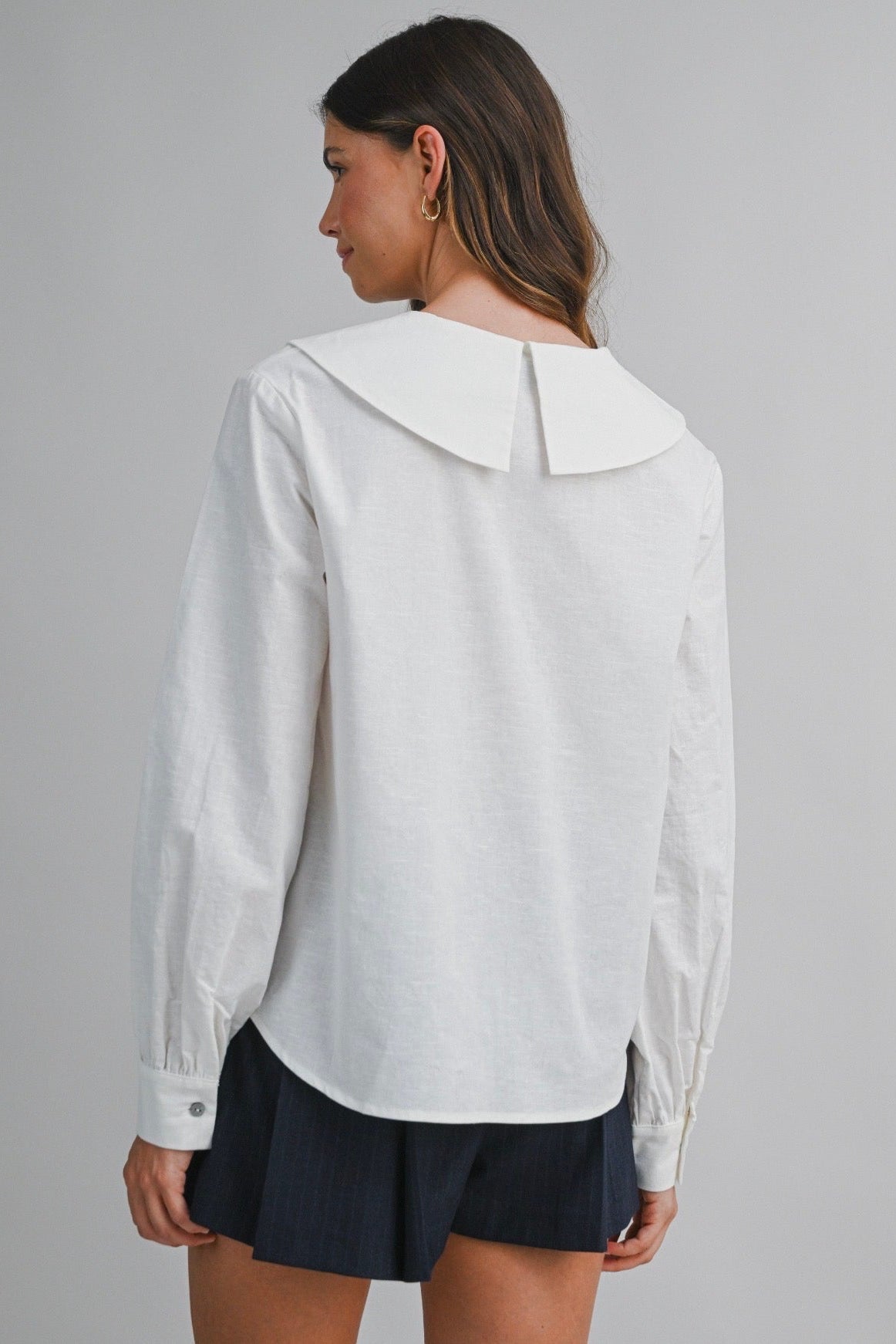 Woman wearing a white blouse with a collar on a gray background