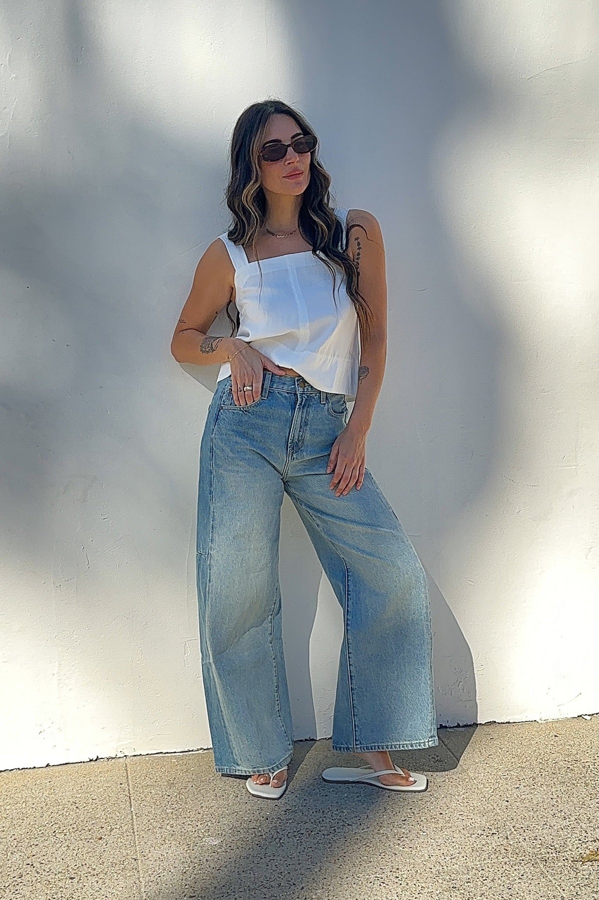 Woman wearing a white top and blue jeans against a plain background