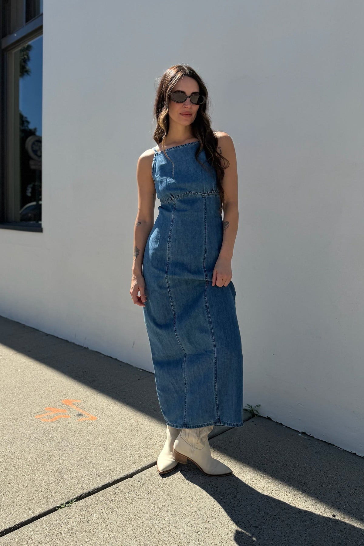 Woman wearing a blue denim dress standing against a white wall.