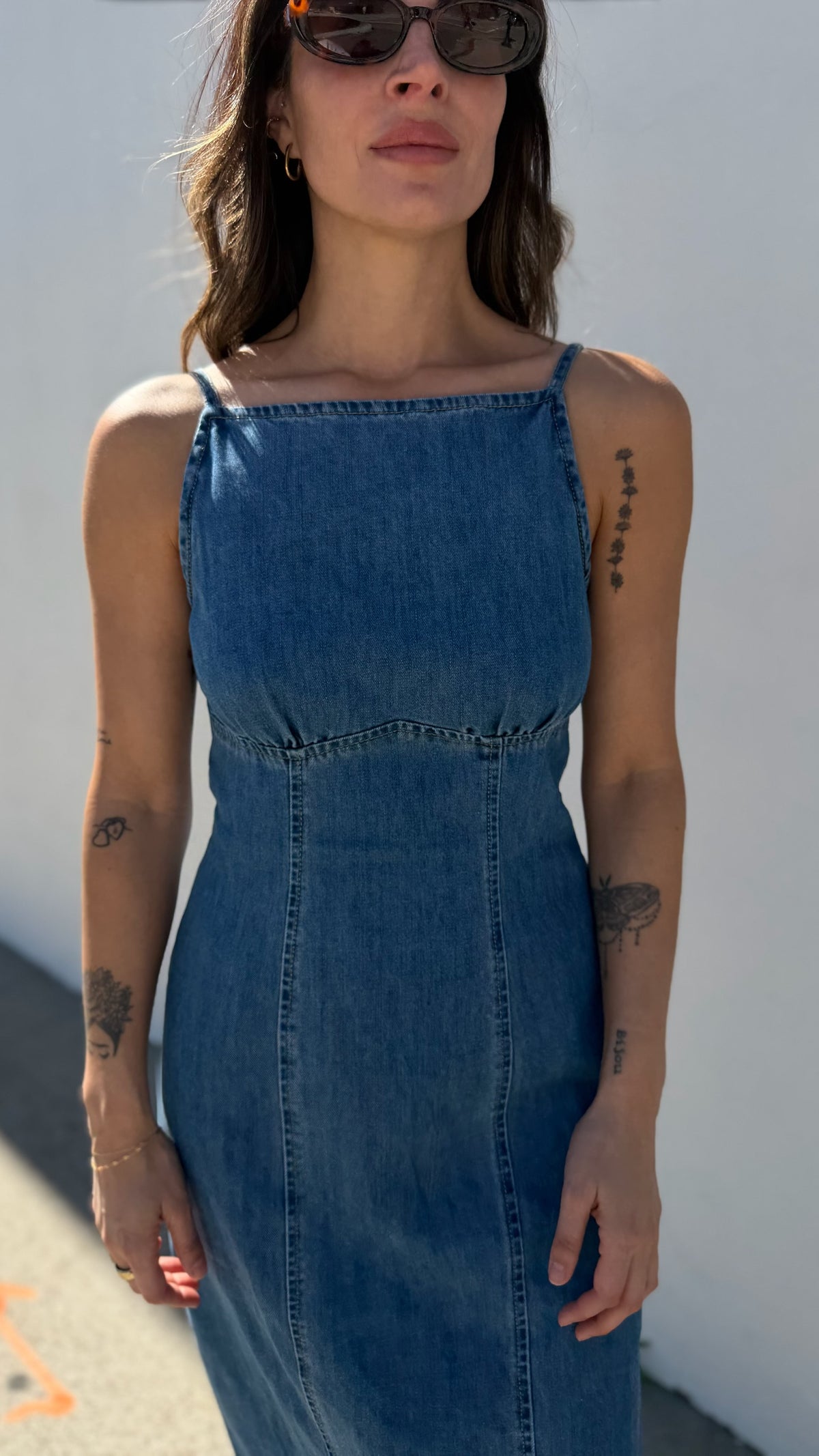Woman wearing a blue denim dress against a white wall.