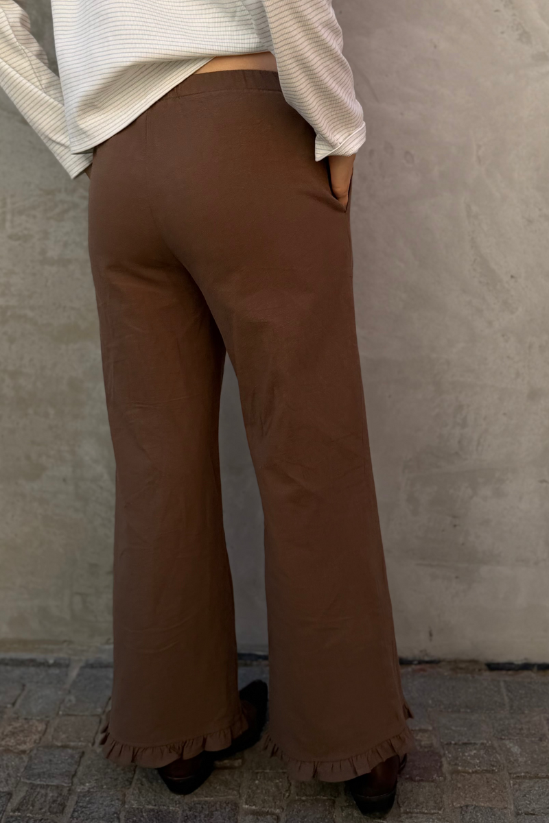Person wearing brown flared pants and a white top against a plain wall.