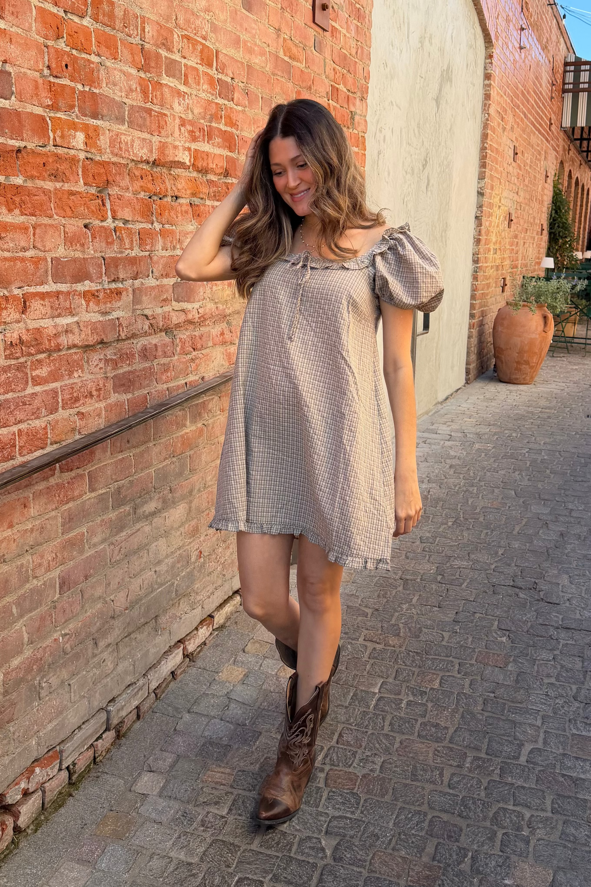 Woman in a light dress and boots walking along a brick wall.