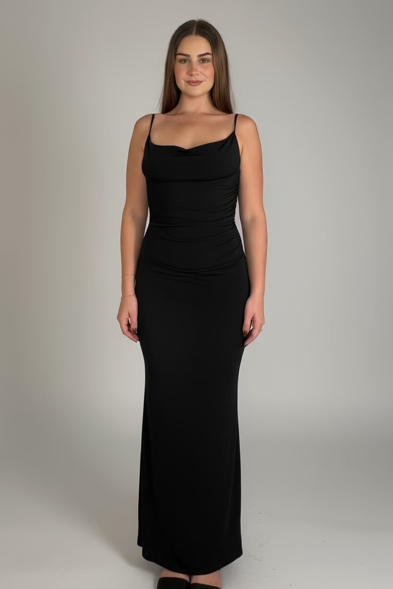 Woman wearing a black dress standing in a room with patterned curtain and wooden floor.