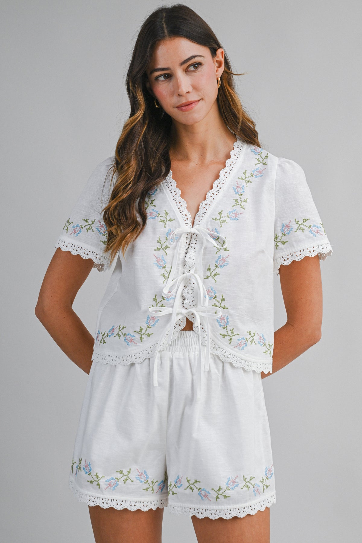 Woman wearing a white embroidered romper on a gray background