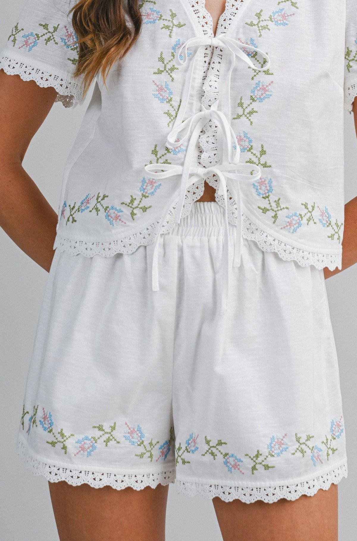 Woman wearing a white embroidered romper on a gray background
