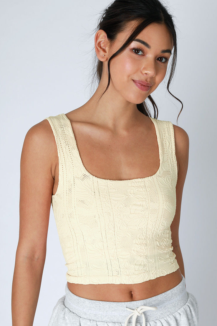 Woman wearing a light yellow sleeveless top and gray pants against a white background