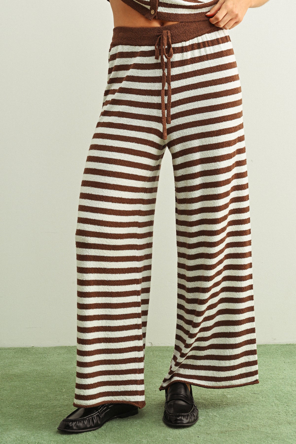 Brown and white striped pants worn by a person on a green floor.