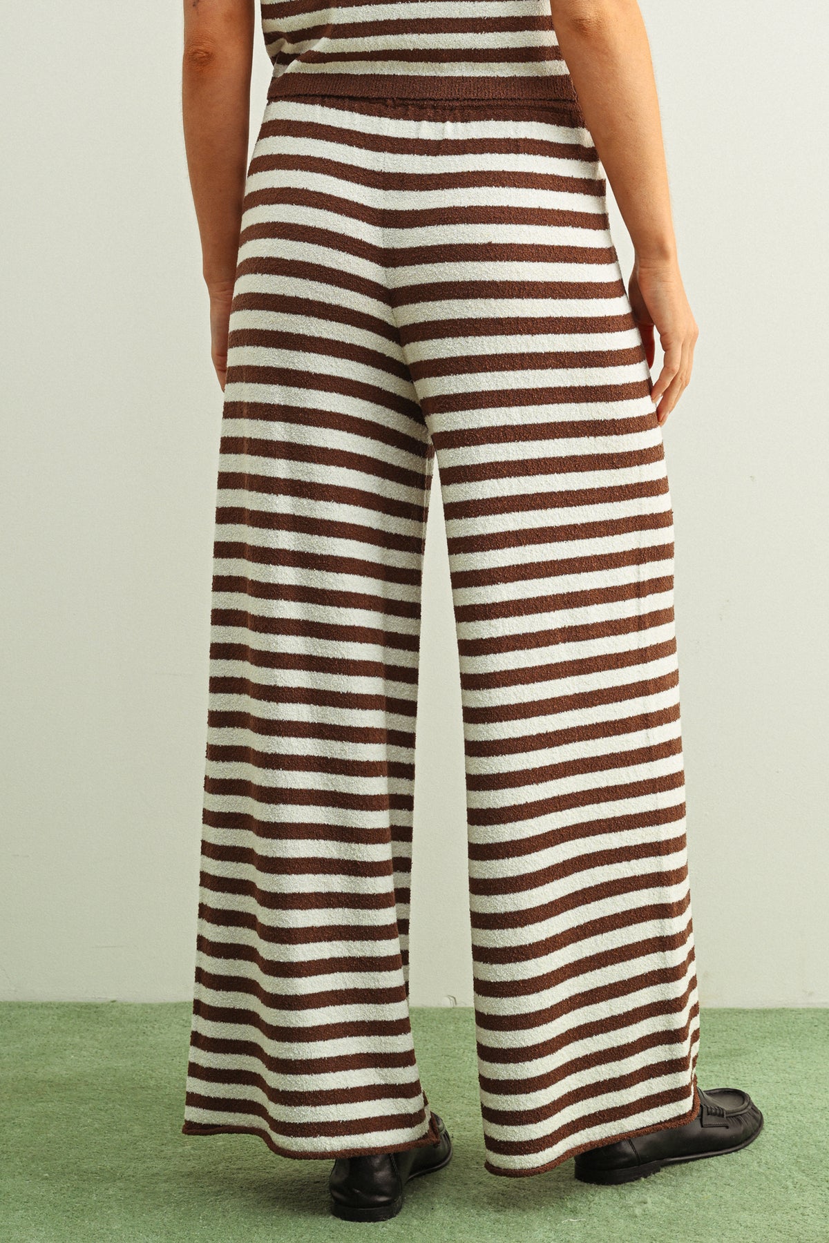 Person wearing a brown and white striped jumpsuit on a green floor with a light gray wall background