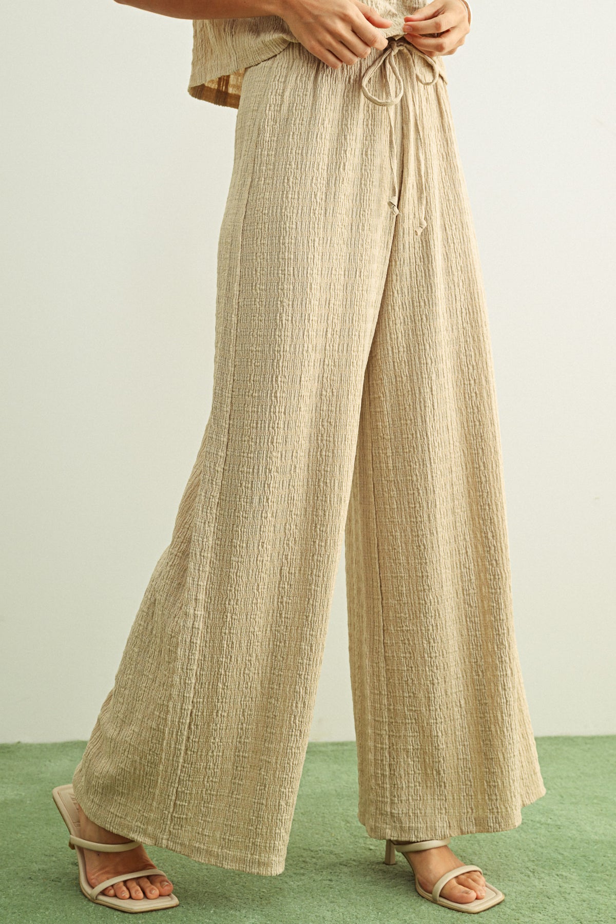 Beige wide-leg pants worn by a person on a green floor with a white wall background