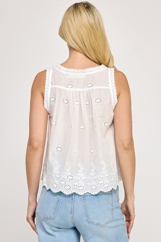 A woman viewed from the back wearing a white sleeveless eyelet lace top and light blue jeans against a plain light gray studio background.