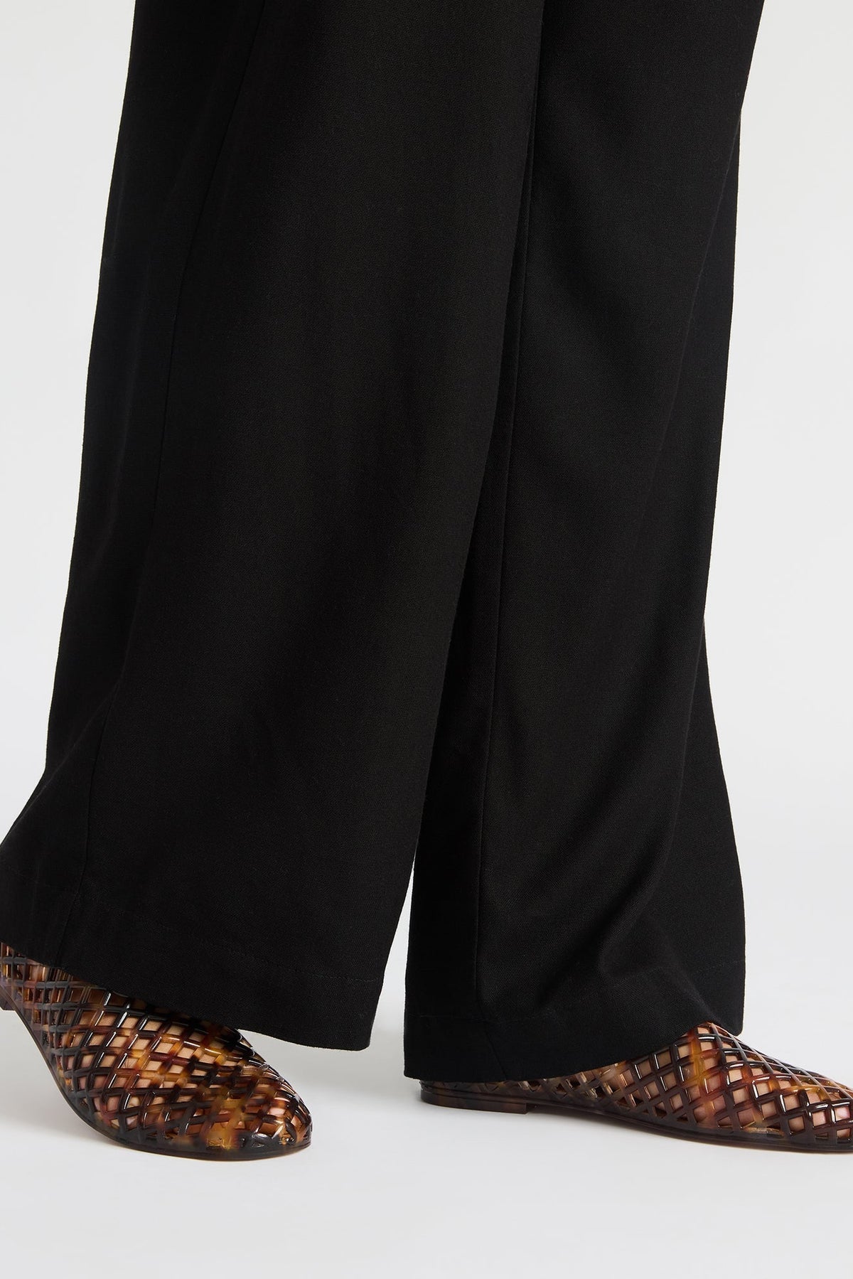 Person wearing black pants and brown woven shoes on a white background