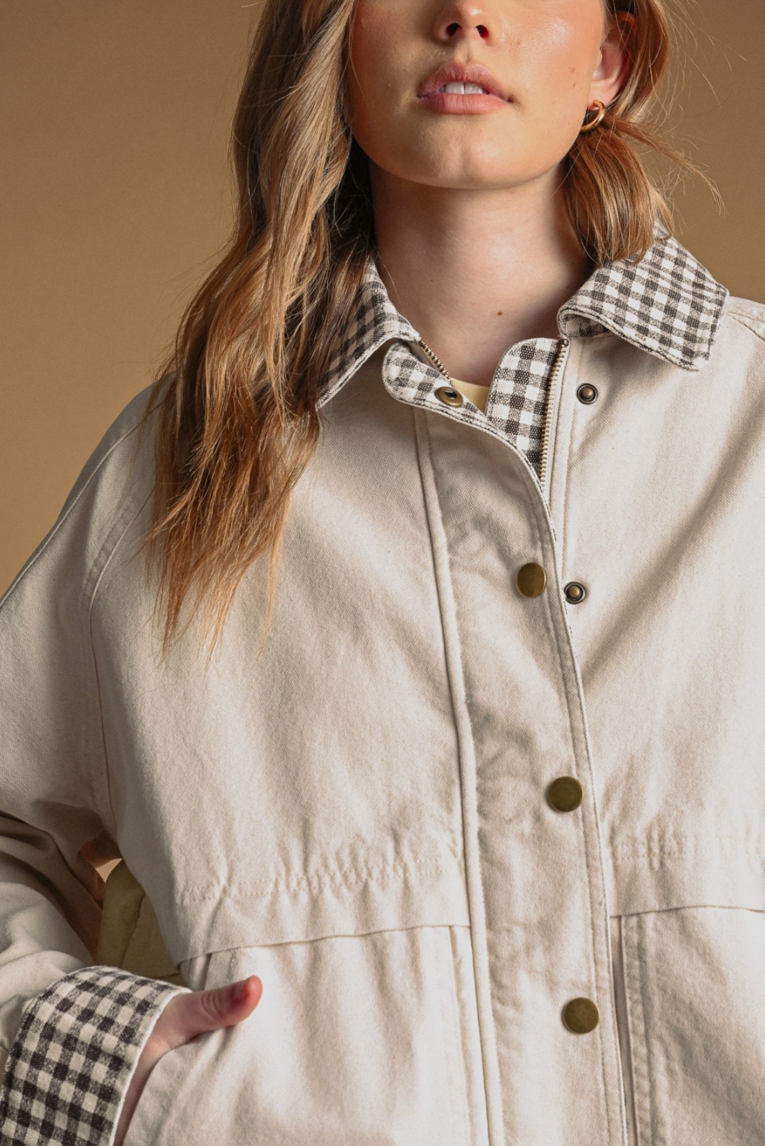 Person wearing a beige jacket with plaid collar and cuffs against a neutral background