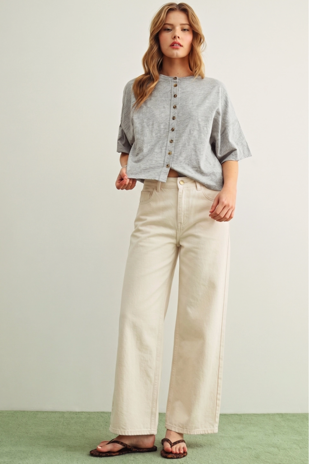 Woman wearing a gray button-up shirt and beige wide-leg pants on a plain background