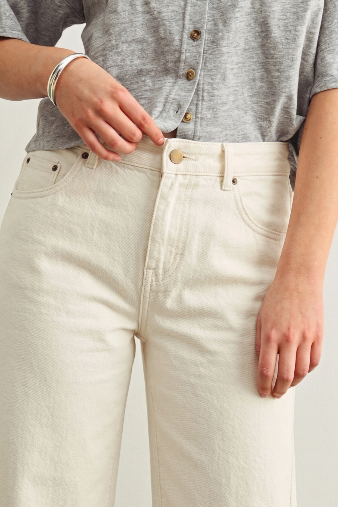 Person wearing a gray shirt and white pants on a plain background