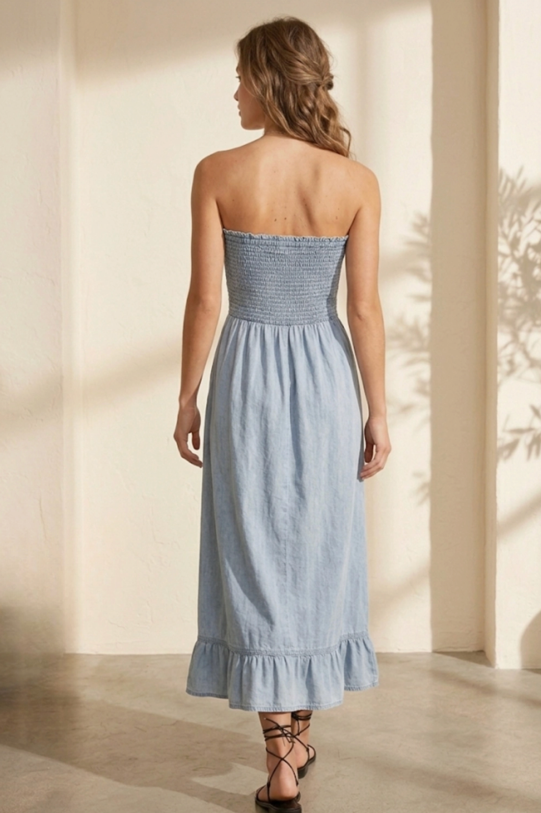 Woman wearing a light blue strapless dress with ruffled hem in a softly lit room.