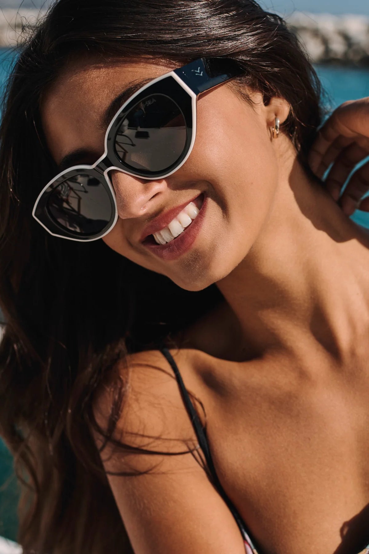 Woman wearing sunglasses and a bikini, smiling with a blurred background