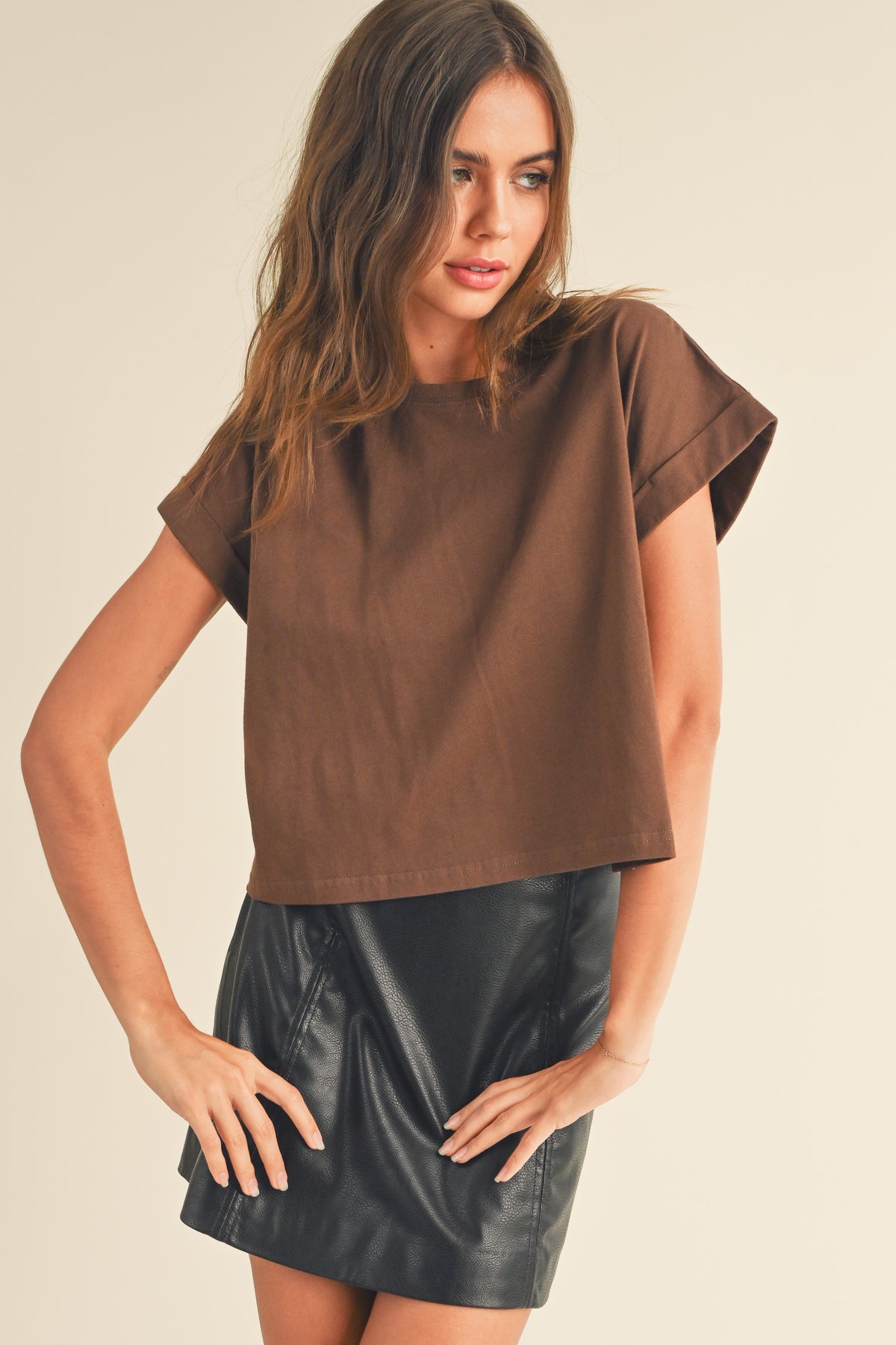 Woman wearing a brown top and black leather skirt on a beige background