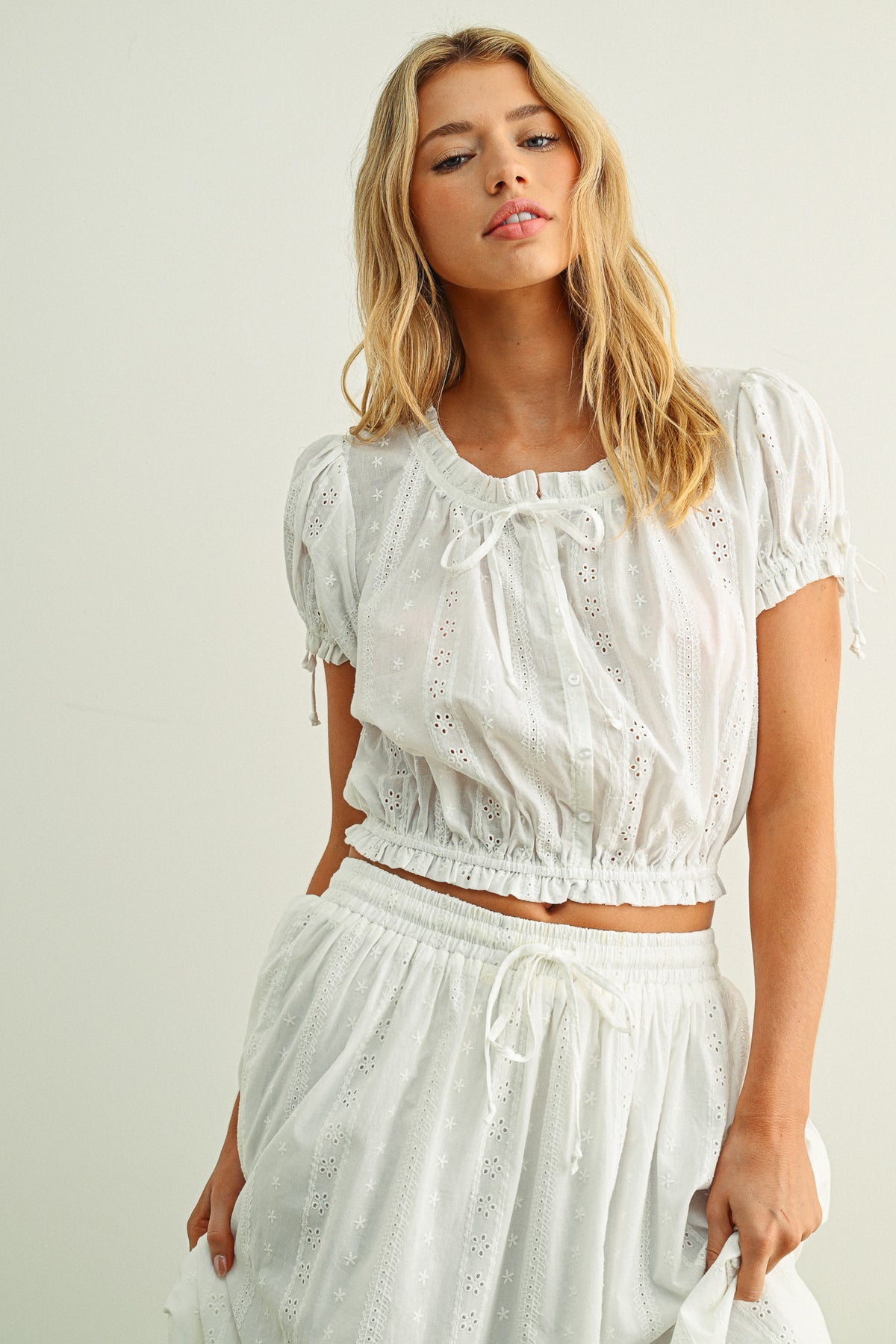 Woman wearing a white embroidered top and skirt set against a plain background