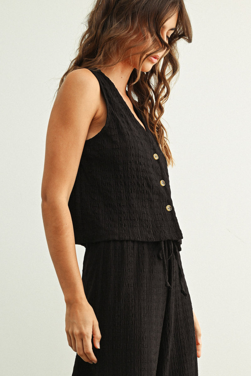 Woman wearing a black sleeveless top with buttons on a plain background