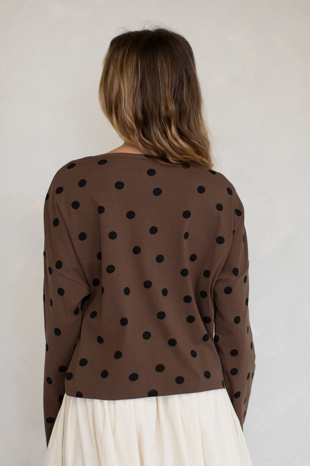 Woman wearing a brown polka dot top against a plain background