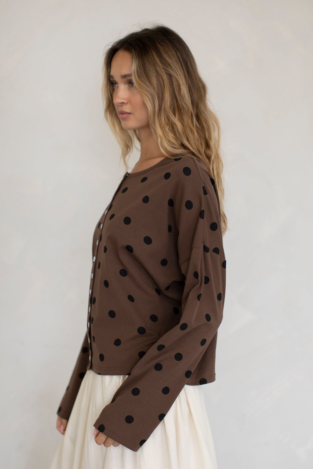 Woman wearing a brown blouse with black polka dots against a plain background