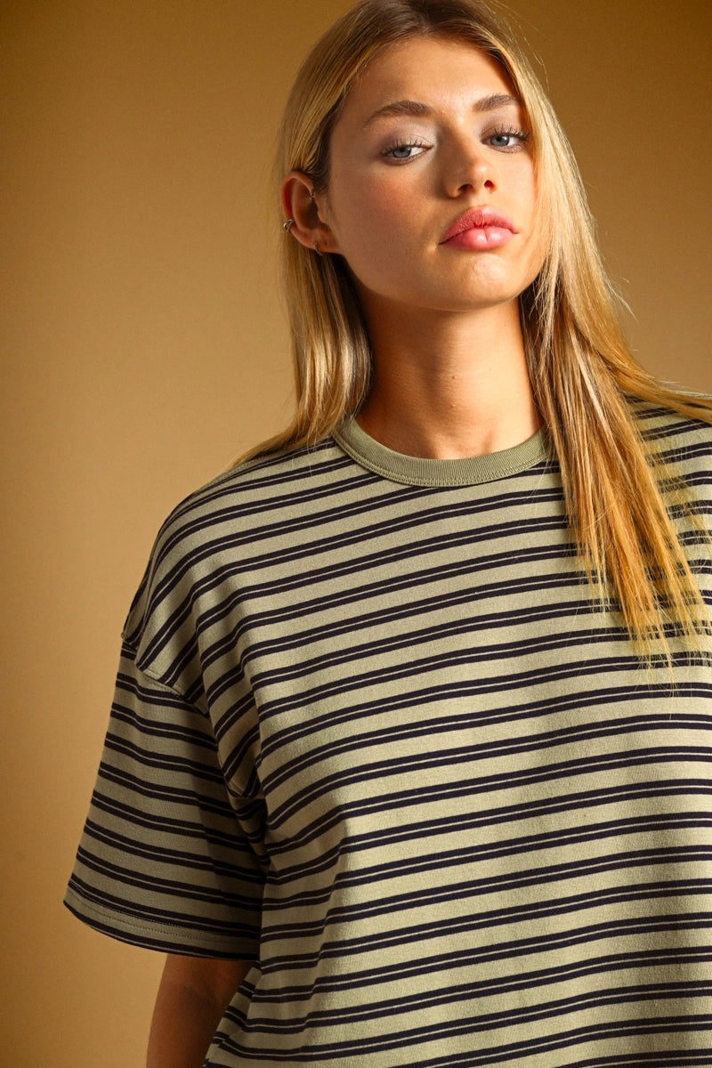 A woman wearing a short-sleeve crewneck t-shirt with thin horizontal black stripes on a beige background, posed against a solid warm brown backdrop.