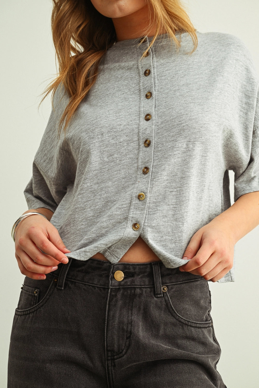 Woman wearing a grey shirt with buttons against a white background.