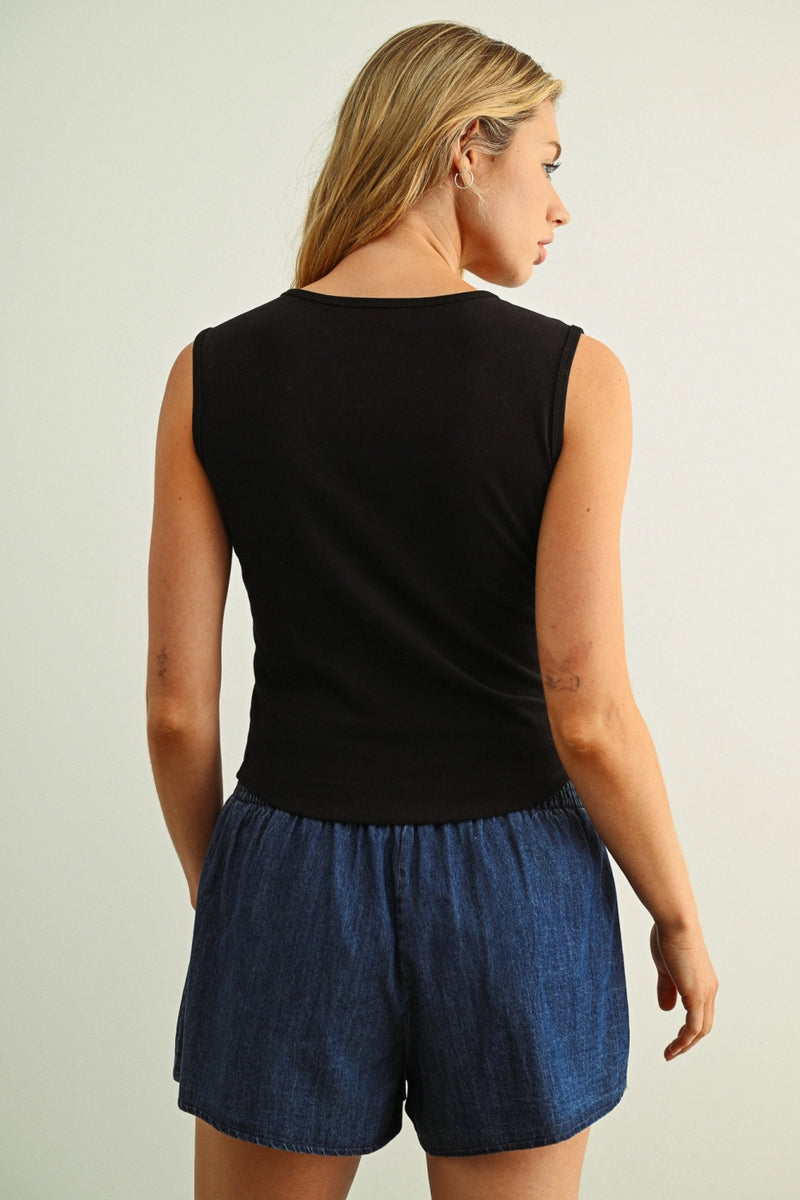 Woman wearing a black sleeveless top and blue denim shorts on a plain background