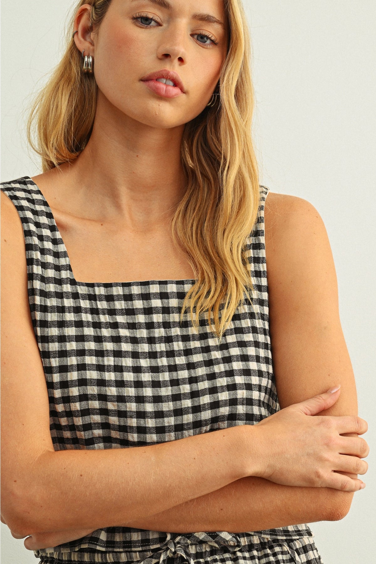 Woman wearing a black and white checkered sleeveless top against a plain background