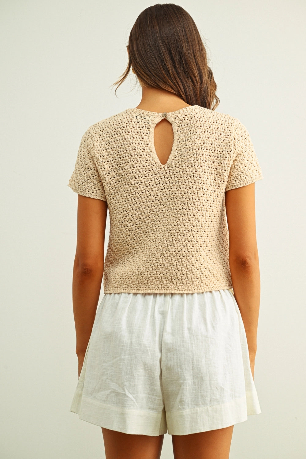 Woman wearing a beige crochet top and white shorts on a plain background
